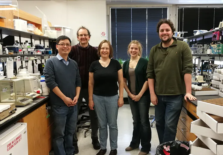 Five lab members standing together between laboratory benches and equipment.